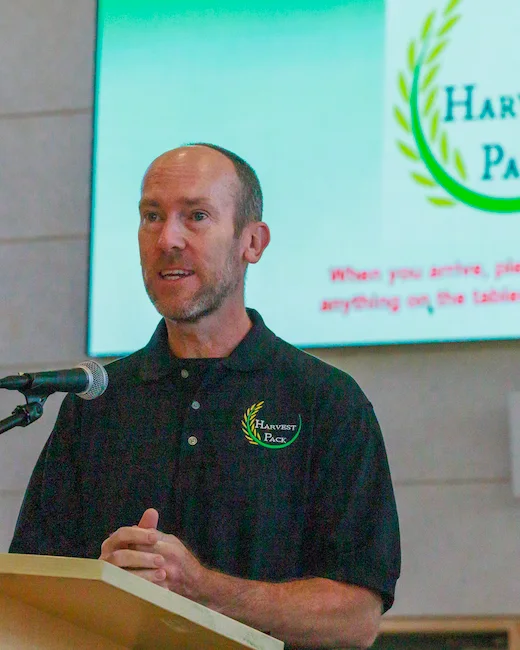 Harvest Pack founder William McNally speaking at the podium during a meal-packing event