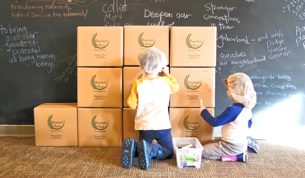 Kids proudly posing with stacks of packed Harvest Pack meal boxes
