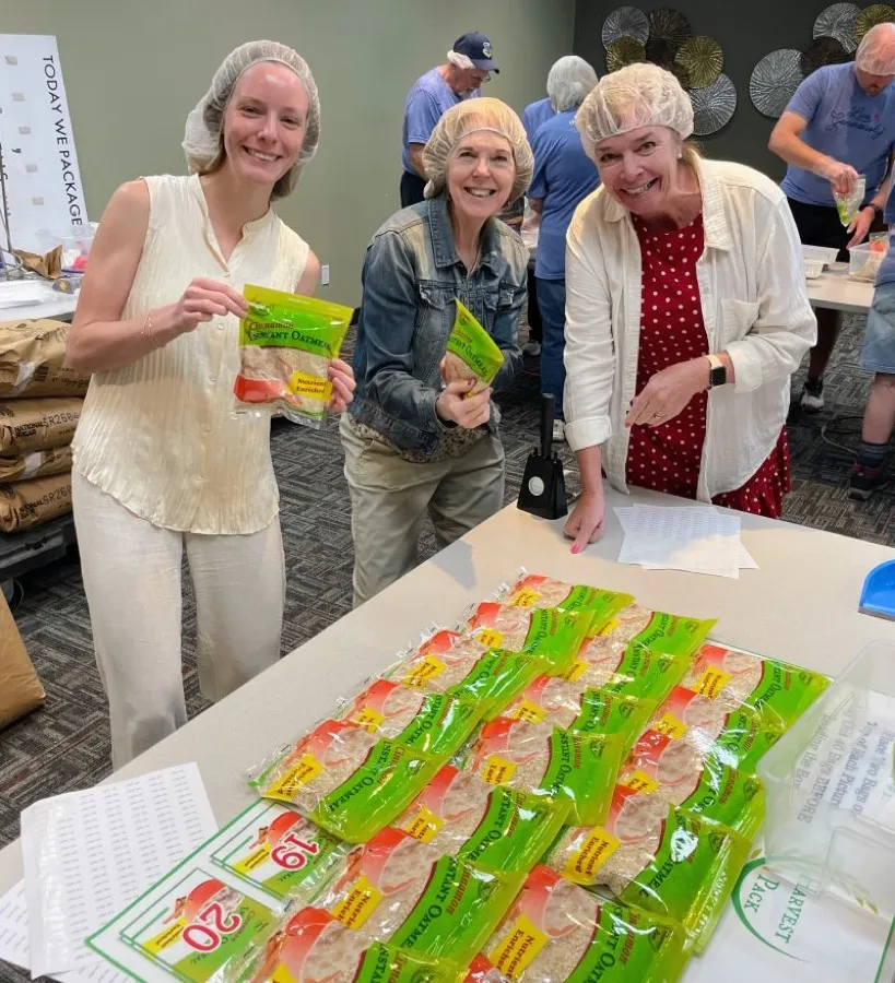 Three laughing volunteers holding finished oatmeal meal bags