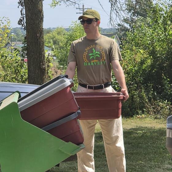 A helper carrying a red bin of collected ingredients to the tractor