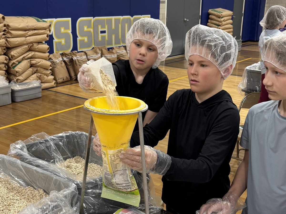 Students in hairnets and gloves filling meal pouches at a school Harvest Pack event